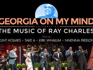 The stars of Georgia on my mind are on stage singing and performing. Above them is text naming the acts of the show and it's title. Above the text, an image of Ray Charles sits proudly above the performers of the show.