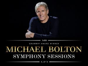 Michael Bolton sits arms-crossed on a black background on top of the logo for his tour that reads "Grammy-award Winner Michael Bolton - Symphony Sessions" in white and gold colors.